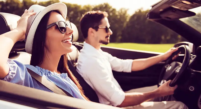A man and woman driving in a convertable