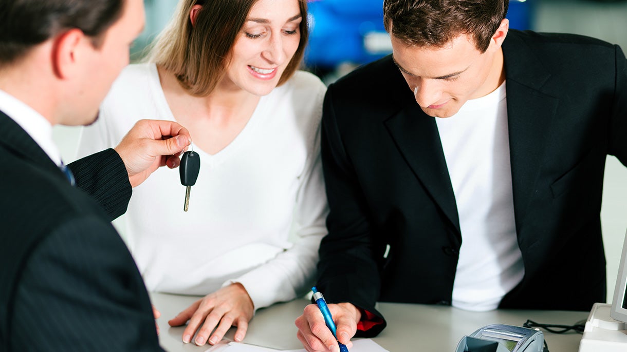 A man and woman going over paperwork with dealer who is handing them keys