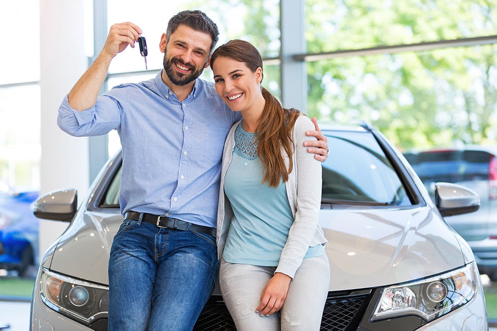 A happy man and woman holding up keys to a new car
